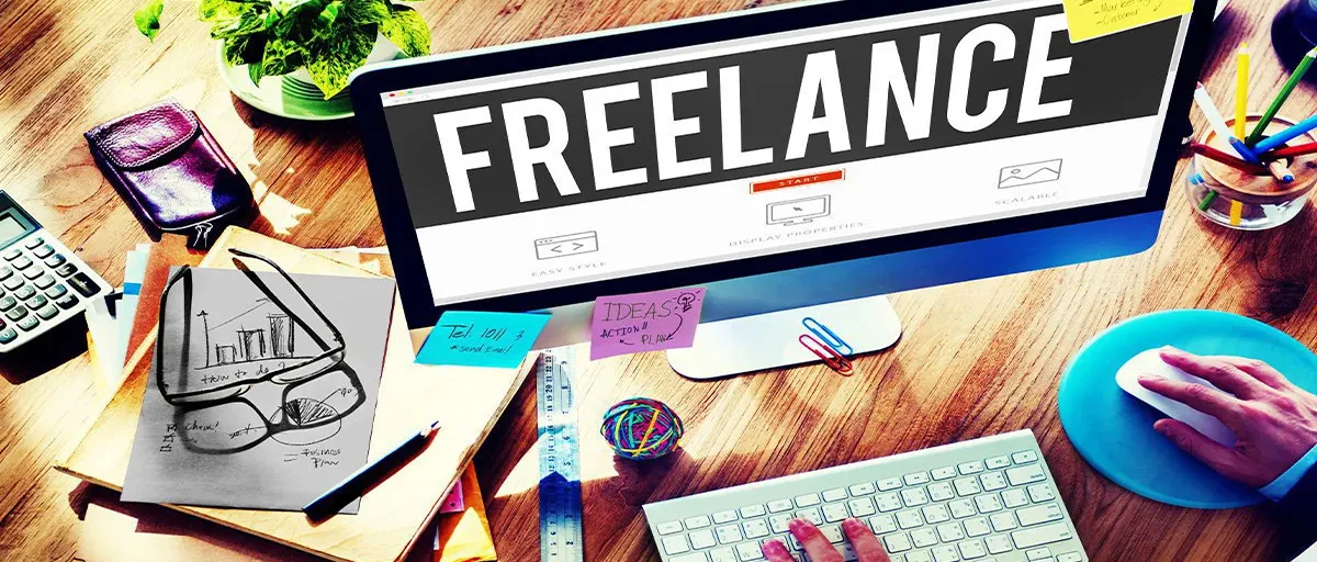 Bilgisayar; klavye üzerinde bir el, ekranda "FREELANCE" yazısı